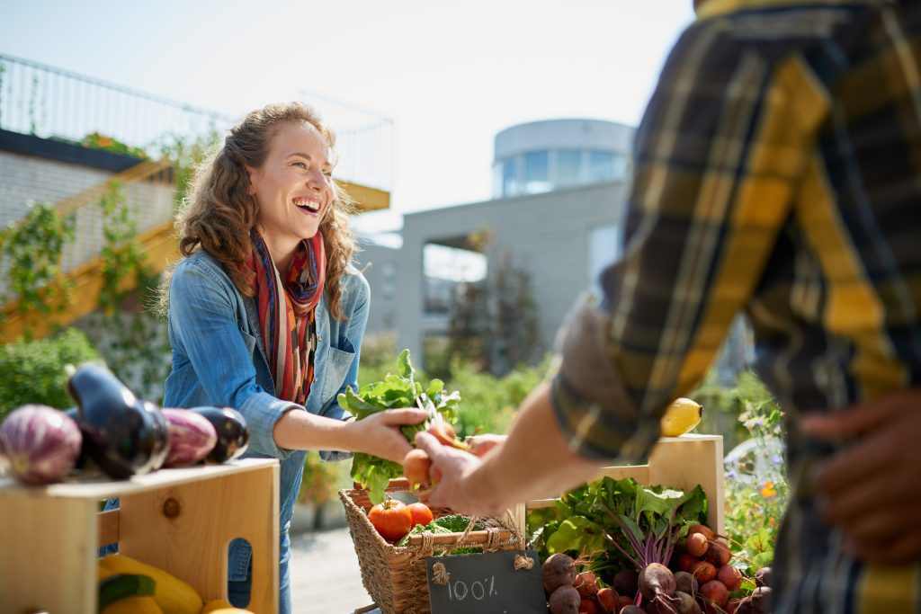 A smiling woman hands carrots from a community garden to a customer