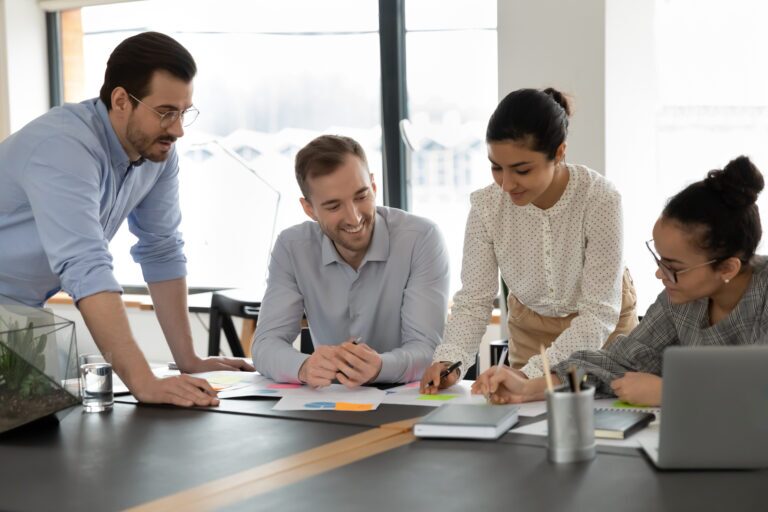 A team of professionals uses our communication skills course to communicate effectively and get more done. Two men and two women collaborate at a desk.