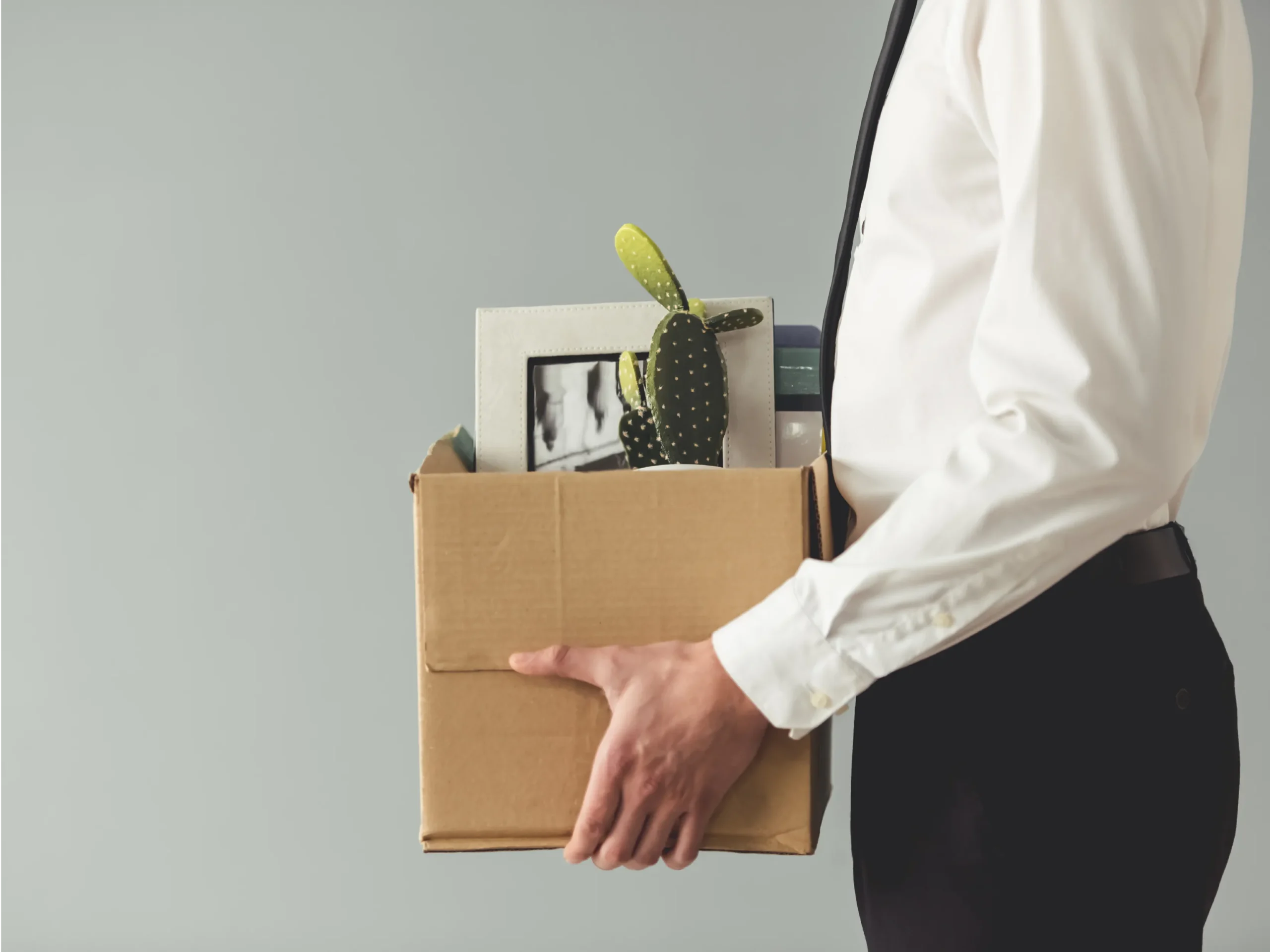 A recently fired office worker holds a box full of belongings from their desk.