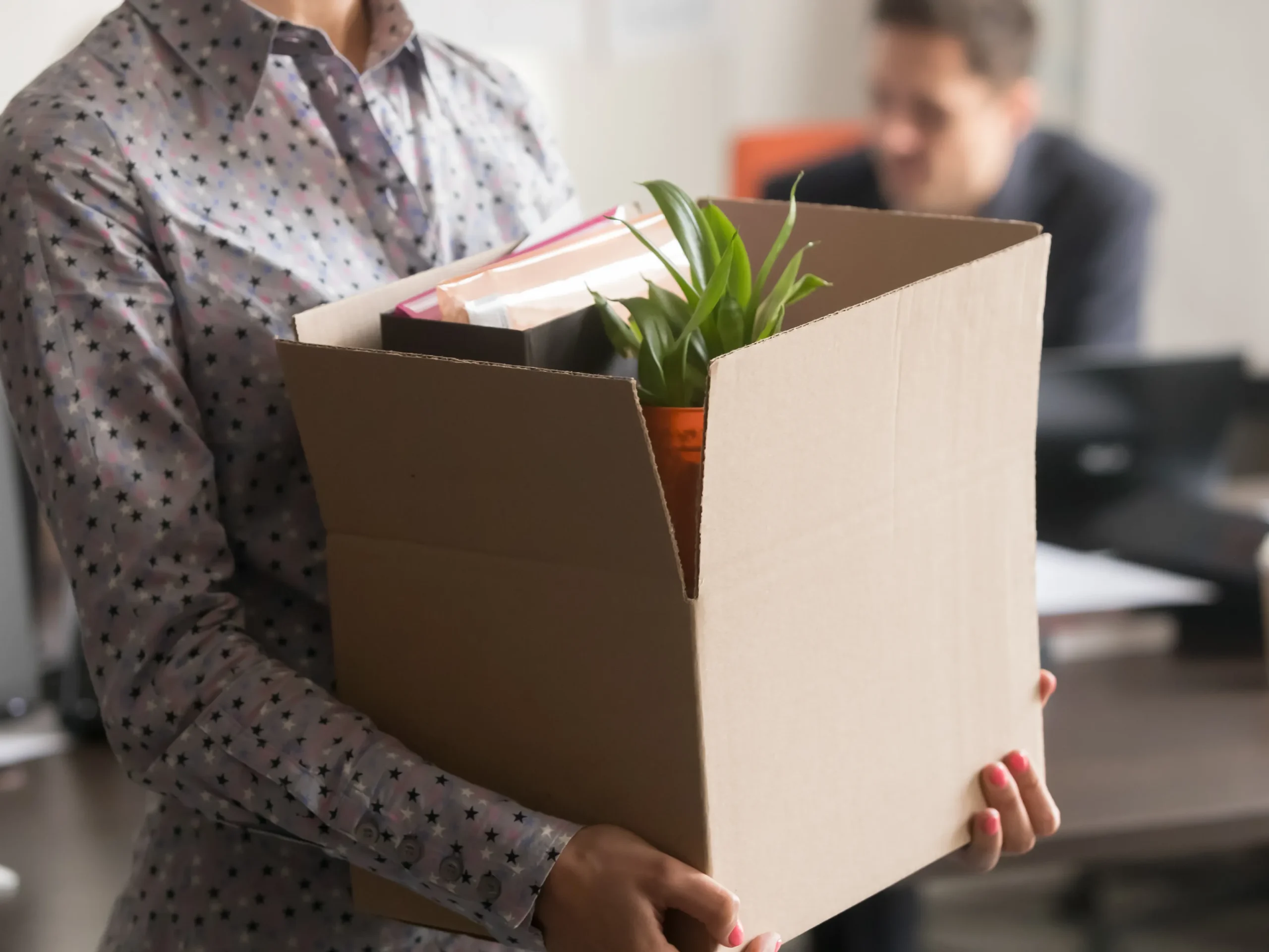 An office worker carries a box of items from their desk.