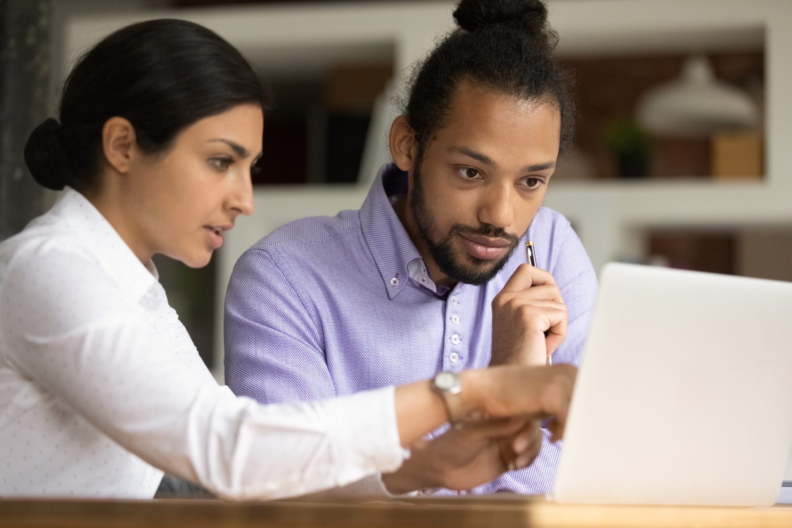 Two colleagues review a document on a laptop - one colleague points to the screen while the other looks closely