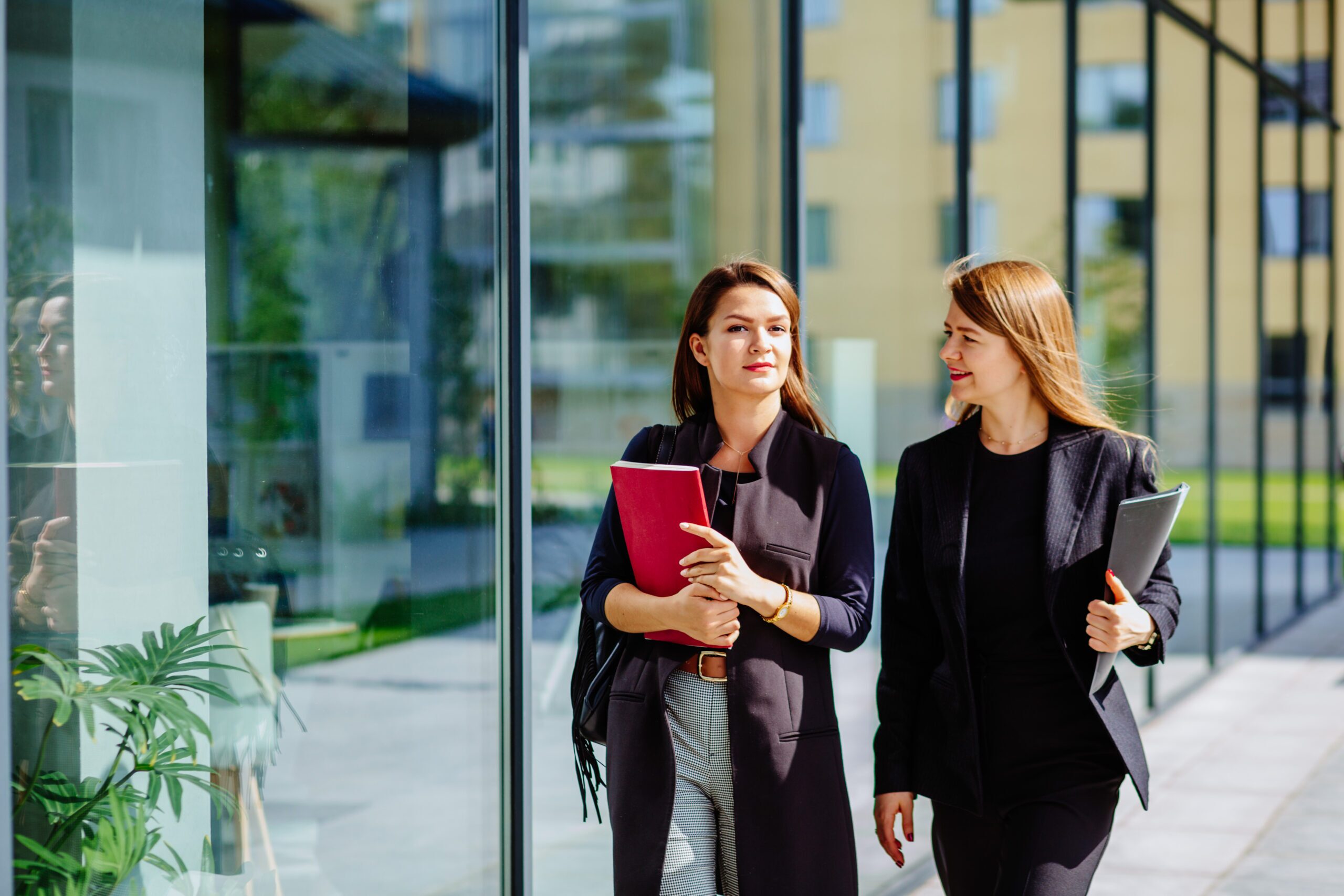 Two colleagues from a government department walk in front of a glass-fronted office building. They are carrying folders that contain policy documents