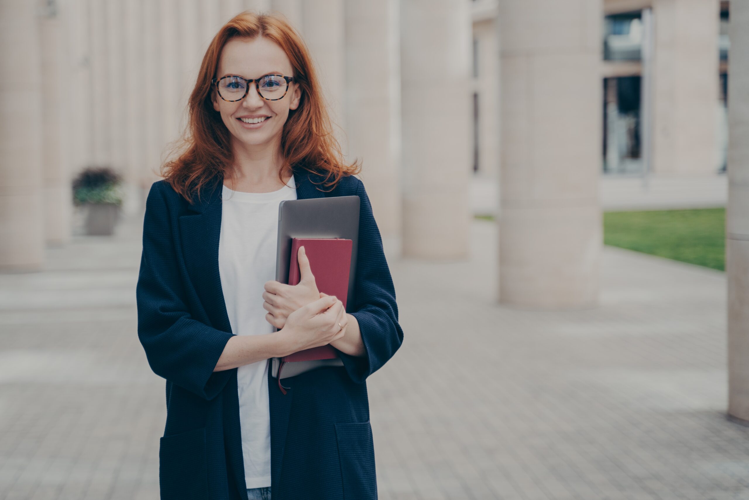 A professional stands outside a government building and carries writing resources for their government job.