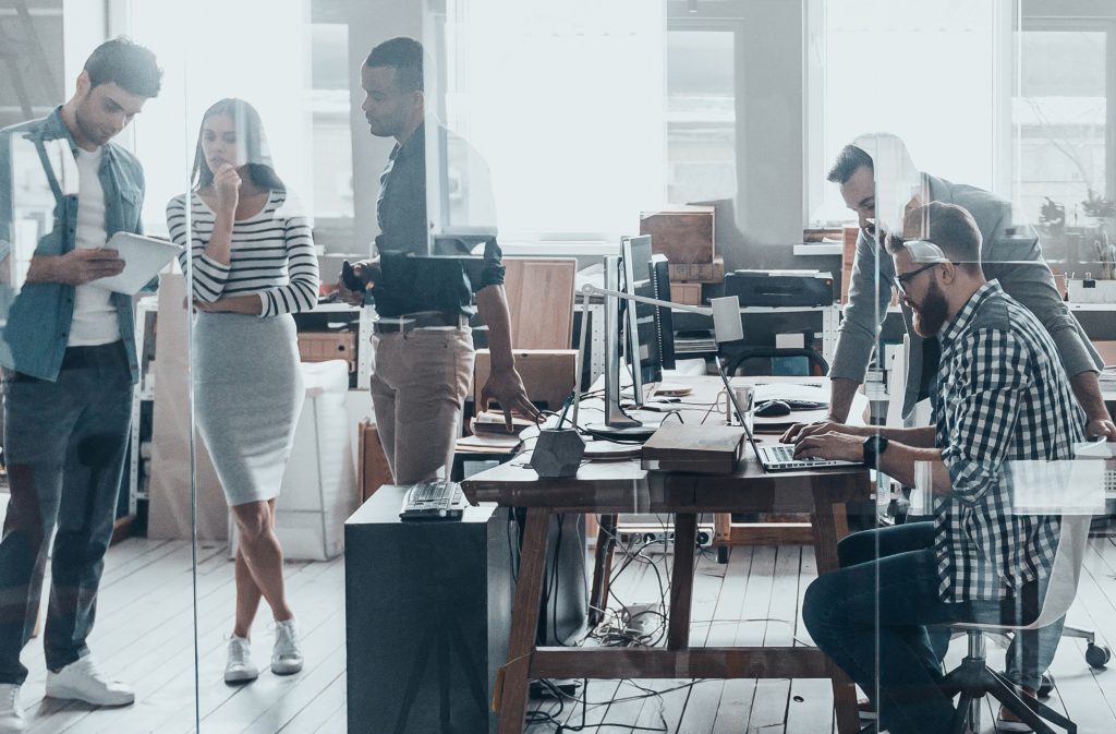 Staff chat and work together in a modern glass office.